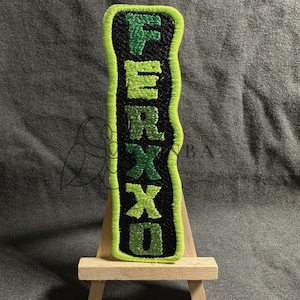 May include: A black and green embroidered patch with the word "FERXXO" written vertically in green letters with a black outline.