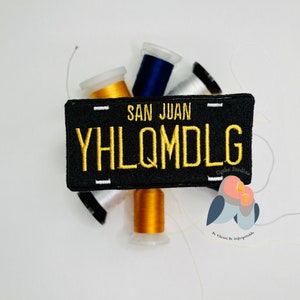 May include: Black and white embroidered patch with the text "SAN JUAN" and "YHLQMDLG" in yellow thread. The patch is surrounded by spools of thread in white, blue, and gold.