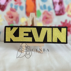 May include: Black fabric patch with the name "KEVIN" embroidered in gold thread.