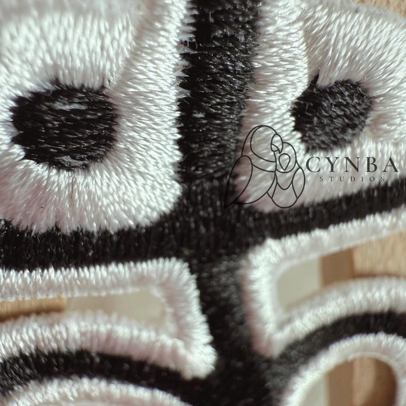 May include: Close-up of a detailed embroidered design in black and white. The stitching creates a textured pattern with rounded shapes and linear elements. The logo "CYNBA STUDIOS" is visible in the upper right corner.