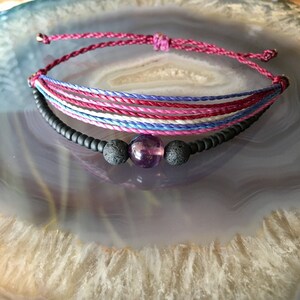 May include: A multi-colored string bracelet with a purple amethyst bead and black lava beads.