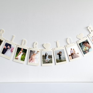 May include: A white string of paper photo frames with the word "Bride & Groom" spelled out in white letters. Each frame contains a wedding photograph.