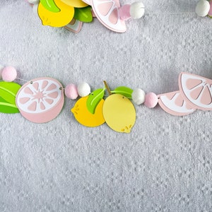May include: A pink and yellow paper garland with lemons and grapefruits, alternating with white and pink pom-poms.