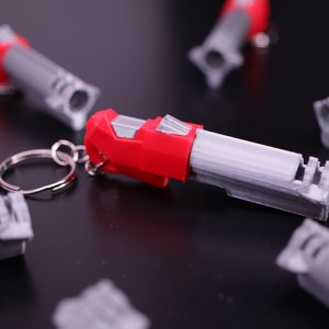May include: A set of six red and gray whistle keychains. The keychains are made of plastic and have a silver key ring.