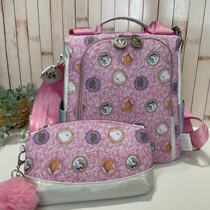 Puede incluir: Mochila rosa y blanca con una bolsa de cosméticos a juego rosa y blanca. La mochila tiene una cremallera blanca y una correa rosa. La bolsa de cosméticos tiene una cremallera blanca y un llavero de pompón rosa.