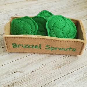 May include: A brown felt box with the words "Brussel Sprouts" embroidered on the front. The box is filled with five green felt brussel sprouts.