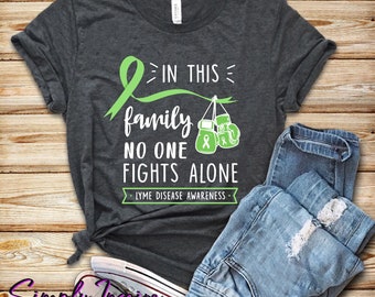 May include: A dark gray t-shirt with a green ribbon and boxing gloves. The text on the shirt reads "In this family no one fights alone. Lyme Disease Awareness."