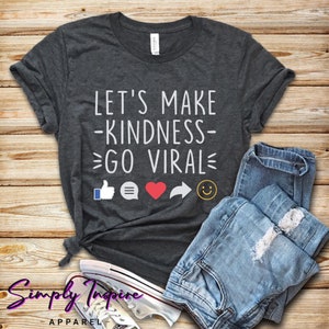 Peut inclure: Un t-shirt gris foncé avec le texte "Let's Make Kindness Go Viral" en blanc. Le t-shirt présente également des icônes de médias sociaux, notamment un pouce en l'air, une bulle de discussion, un cœur, une flèche de partage et un smiley.