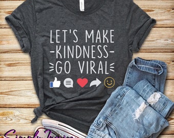 May include: A dark gray t-shirt with the text "Let's Make Kindness Go Viral" in white. The shirt also features social media icons including a thumbs up, a chat bubble, a heart, a share arrow, and a smiley face.