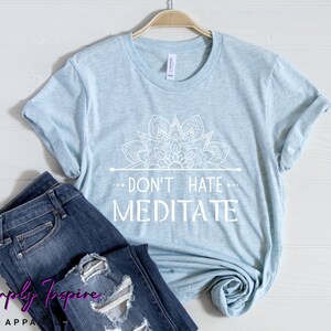K&ouml;nnte beinhalten: Ein hellblaues T-Shirt mit einem wei&szlig;en Mandala-Design und dem Text "...Don't Hate... Meditate" auf der Vorderseite.
