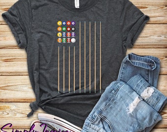 Puede incluir: Una camiseta gris oscuro con un diseño de bandera de billar. La bandera está compuesta por bolas de billar y tacos de billar. Las bolas están numeradas del 1 al 15 y la bola blanca.