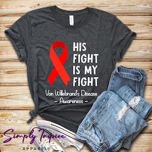 May include: A dark grey t-shirt with a red ribbon and white text that reads "His Fight Is My Fight Von Willebrand's Disease - Awareness - "