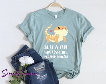 Könnte beinhalten: Ein hellblaues T-Shirt mit einem Comic-Bartagamen und dem Text "Just a girl who loves her bearded dragon".