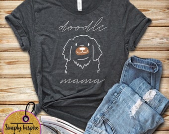 Può includere: Una maglietta grigio scuro con il testo "doodle mama" in lettere bianche. Un contorno bianco di un cane barboncino marrone è centrato sulla maglietta.