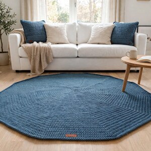 Peut inclure: Un grand tapis circulaire en crochet bleu avec un motif de points rayonnants texturés. Le tapis présente une petite étiquette rectangulaire de couleur marron semblable à du cuir sur le bord, avec une construction en fil faite main.