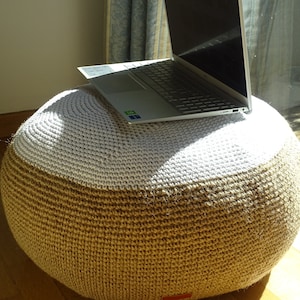 May include: A round, crocheted footstool with a white top and a brown bottom. A silver laptop computer is resting on the top of the footstool.
