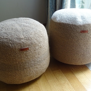 Könnte beinhalten: Zwei runde, gewebte Poufs in neutralen Tönen. Einer ist ganz hellbraun, während der andere eine weiße Oberseite hat. Jeder hat ein kleines braunes Lederetikett. Die Poufs stehen auf einem Holzboden, was auf ein Wohnkultur-Thema hindeutet.