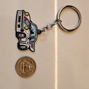 May include: A white, blue, and red car keychain with a silver chain and ring. The car is a vintage race car with a number 6 on the side. The keychain is about the size of a US quarter.