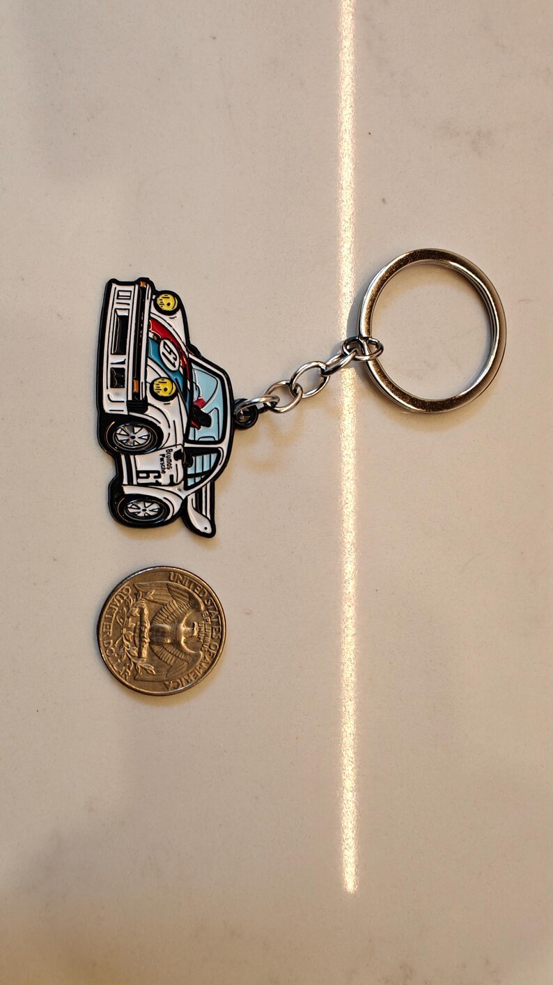 May include: A white, blue, and red car keychain with a silver chain and ring. The car is a vintage race car with a number 6 on the side. The keychain is about the size of a US quarter.