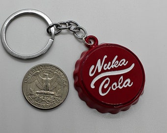 May include: A red Nuka Cola bottle cap keychain with white lettering. The keychain includes a silver key ring and chain. A US quarter is next to the keychain for size comparison.
