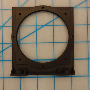 May include: A dark brown, square-shaped 3D printed mounting bracket featuring a large circular center cutout with eight small screw holes positioned around the perimeter. The bracket measures approximately 4 inches in width and height.