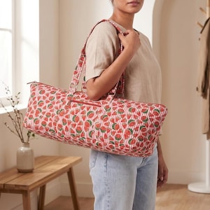 Könnte beinhalten: Eine rechteckige, gesteppte Reisetasche mit einem sich wiederholenden Muster aus Wassermelonenstücken auf einem Hintergrund aus dünnen, roten und weißen vertikalen Streifen. Die Tasche hat zwei lange Schulterriemen und eine Reißverschlusstasche.