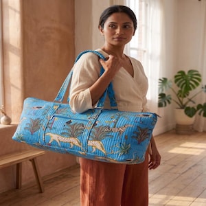 Könnte beinhalten: Eine gesteppte Reisetasche in leuchtendem Blau mit einem sich wiederholenden Muster aus Leoparden, Zebras und tropischen Palmen. Die Tasche verfügt über zwei lange Schulterriemen, eine horizontale Außentasche mit Reißverschluss und eine rechteckige Form.