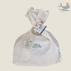 Peut inclure: Un sac en coton blanc avec un logo de baleine et le texte "ZERO WASTE" imprimé dessus. Le sac est attaché avec de la ficelle et porte une étiquette avec le texte "Baleia Vulcanica" et un logo de baleine.