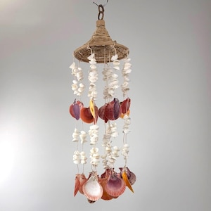 May include: A hanging seashell mobile with a woven top. The mobile features strands of white and colourful seashells, including shades of orange, purple, and pink. The mobile is suspended from a metal hook.