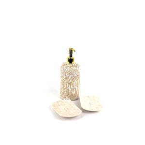 May include: A beige bathroom set comprising a soap dispenser with a gold pump and two soap dishes. The dispenser and dishes have a textured finish. The set is designed with a neutral colour scheme.