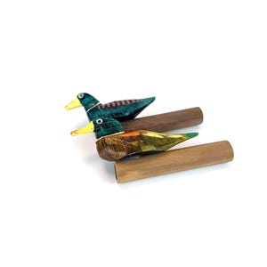 May include: Two hand-painted wooden duck figurines. The ducks have green, brown, yellow, and blue coloring. The ducks are perched on brown wooden dowels. The ducks are decorative and are likely used as home decor.