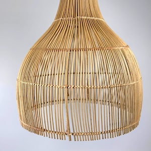 May include: A natural-toned, woven rattan pendant light fixture. The light has a bell-shaped design with a wide base and a narrower top, suspended by a metal hook. The fixture is made of vertical rattan strips.