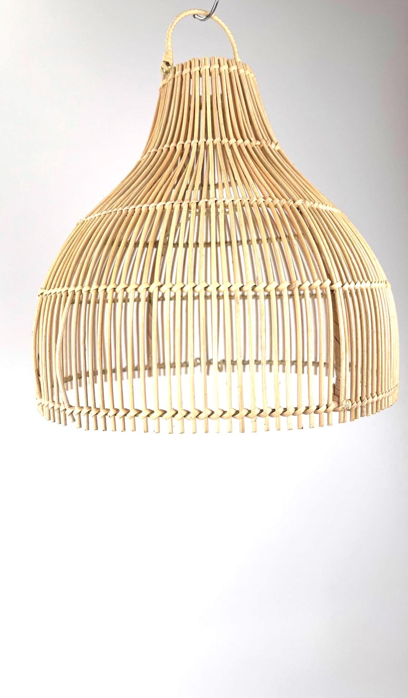 May include: A natural-toned, woven rattan pendant light fixture. The light has a bell-shaped design with a wide base and a narrower top, featuring vertical rattan strips held together by horizontal weaving. The fixture is suspended from a metal hook.