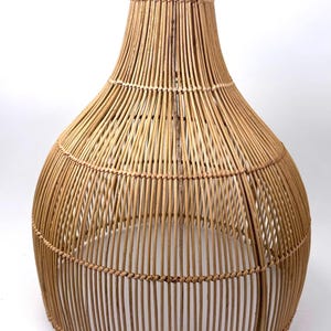 May include: A woven rattan pendant light fixture with a teardrop shape. The natural brown lamp has a handle at the top and is made of vertical and horizontal woven rattan strips. The light fixture is suitable for indoor use.