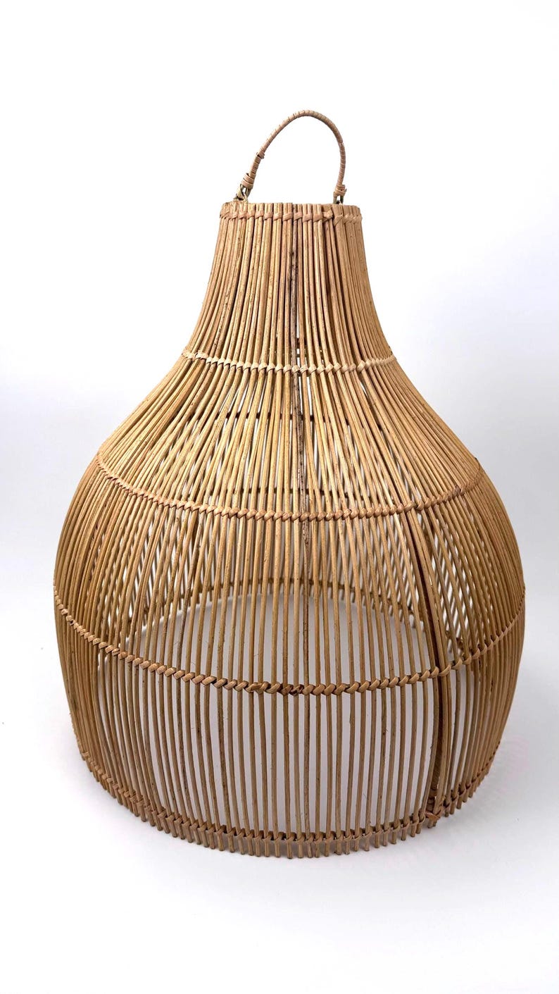 May include: A woven rattan pendant light fixture with a teardrop shape. The natural brown lamp has a handle at the top and is made of vertical and horizontal woven rattan strips. The light fixture is suitable for indoor use.
