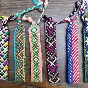 May include: Seven colorful friendship bracelets with various geometric patterns. The bracelets are made with colorful threads and are tied together in a knot.