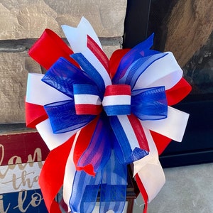 May include: A red, white and blue bow made of ribbon and mesh. The bow is tied in a knot and has a decorative design.