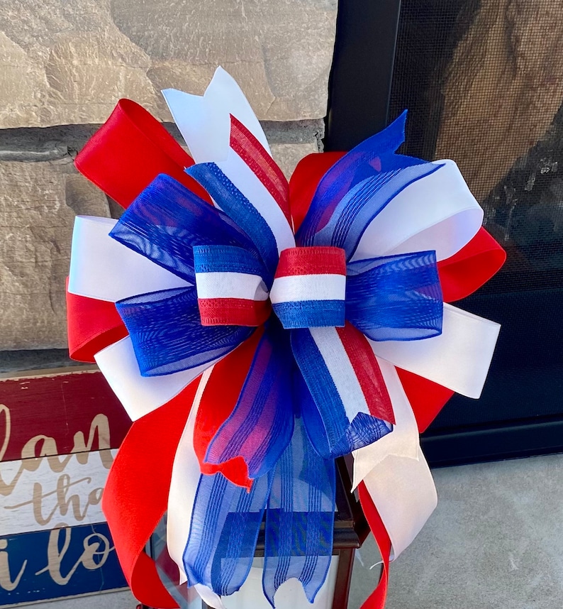 May include: A red, white and blue bow made of ribbon and mesh. The bow is tied in a knot and has a decorative design.
