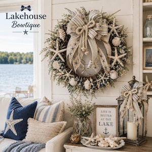 May include: A decorative wreath featuring a grapevine base, green foliage, starfish, and seashells, accented with a large striped ribbon bow. Below, a wooden sign reads "LIFE IS BETTER AT THE LAKE" with an anchor icon, next to a lantern.
