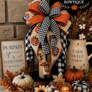 May include: A decorative bow featuring orange and black-and-white buffalo check ribbons with pumpkin prints, displayed on a black lantern. The scene includes a sign reading PUMPKIN spice & EVERYTHING nice, a pitcher labeled FARM SWEET FARM, and pumpkins.