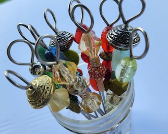 Peut inclure: Un ensemble de huit piques à cocktail en perles colorées dans un bocal en verre transparent. Les piques présentent une variété de perles, notamment transparentes, rouges, vertes et dorées.