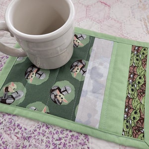 Puede incluir: Posavasos de tela verde y blanco con un patr&oacute;n repetido de un personaje de dibujos animados con casco. El posavasos tiene un borde blanco y verde y est&aacute; sobre una colcha rosa y blanca.