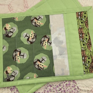 Puede incluir: Dos posavasos de tela verde con un dise&ntilde;o acolchado. Un lado presenta un patr&oacute;n repetido de un peque&ntilde;o personaje verde con casco. El otro lado tiene un borde verde con un patr&oacute;n repetido del mismo personaje.