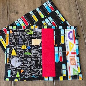May include: A quilted fabric notebook cover with a science theme. The cover features a black background with colorful test tubes, mathematical symbols, and a bright red vertical stripe. The cover is approximately 9 inches by 6 inches.
