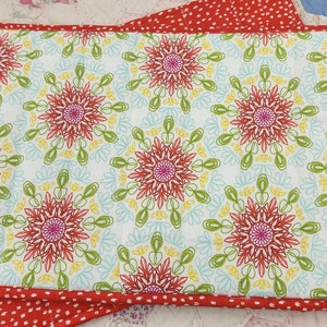 May include: Red and white placemat with a floral pattern. The placemat has a red border with white polka dots.