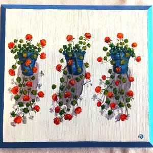 Puede incluir: Pintura cuadrada que presenta tres macetas azules con flores rojas y hojas verdes. Las macetas están sobre un fondo blanco con un borde azul. La pintura tiene una apariencia texturizada.