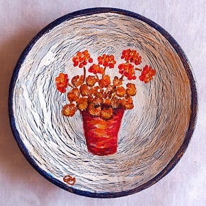 Può includere: Ciotola decorativa dipinta a mano con un motivo floreale. La ciotola presenta un vaso di fiori rosso con fiori arancioni su uno sfondo bianco e blu. Il bordo della ciotola è blu scuro.