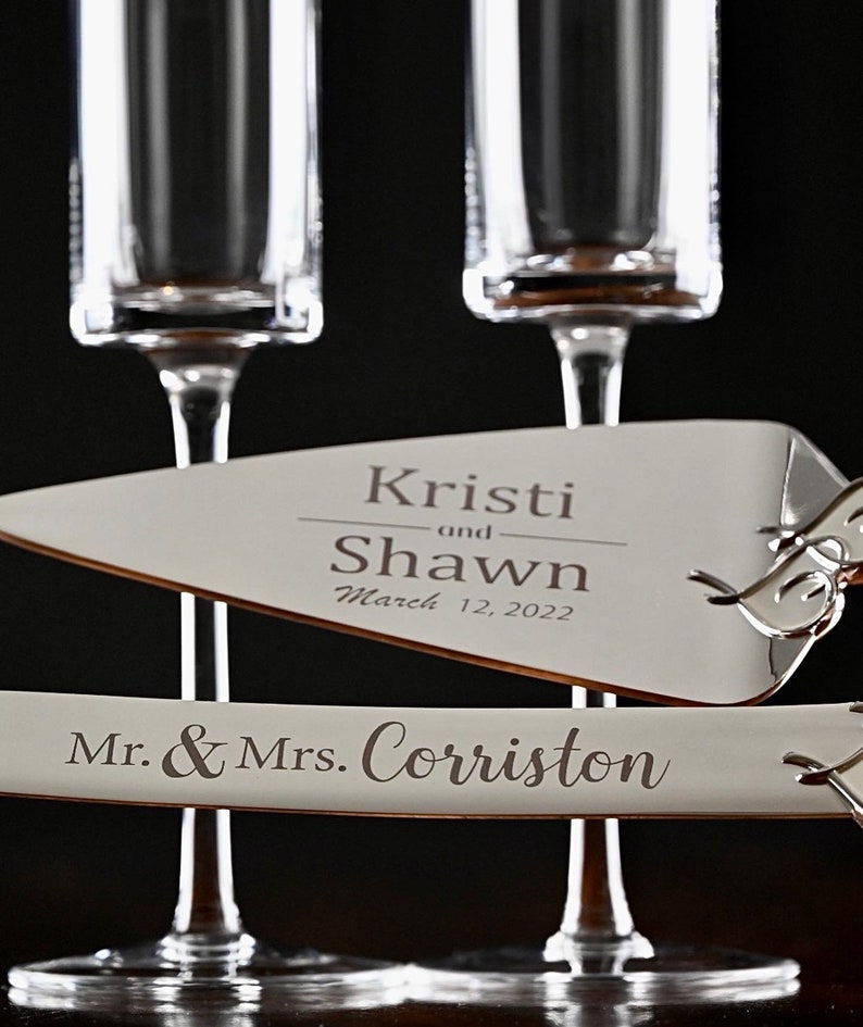 May include: Two champagne flutes and a cake server with the text "Kristi and Shawn March 12, 2022" and "Mr. & Mrs. Corriston" engraved on them.