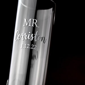 May include: A clear glass champagne flute with the text "MR. lorriston 3.12.22" etched into the side.
