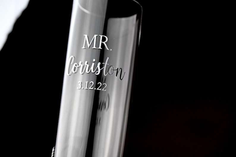 May include: A clear glass champagne flute with the text "MR. lorriston 3.12.22" etched into the side.